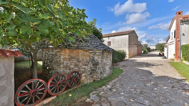 Un bâtiment en pierre avec un toit en pente, un étroit sentier pavé et un arbre aux feuilles vertes.