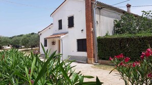 Une maison à deux étages, avec une façade blanche, une cheminée en briques rouges et un toit recouvert de tuiles.