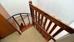 Une chaise en bois avec une structure en métal, placée dans un coin d’une pièce dont le sol est recouvert d’une moquette et les murs sont peints en blanc.