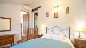 Un dormitorio con cama, mesitas de noche de madera, cómoda y espejo. Hay luces empotradas en la pared y cuadros enmarcados.