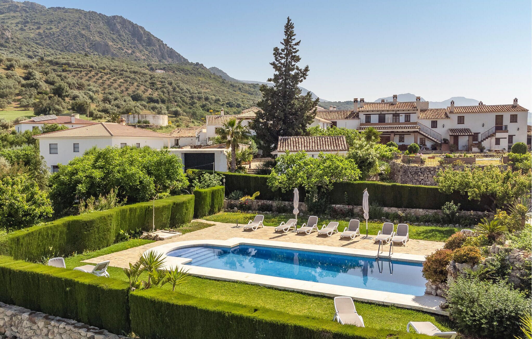 A pool area with lounge chairs, surrounded by well-manicured hedges and a mountainous backdrop.