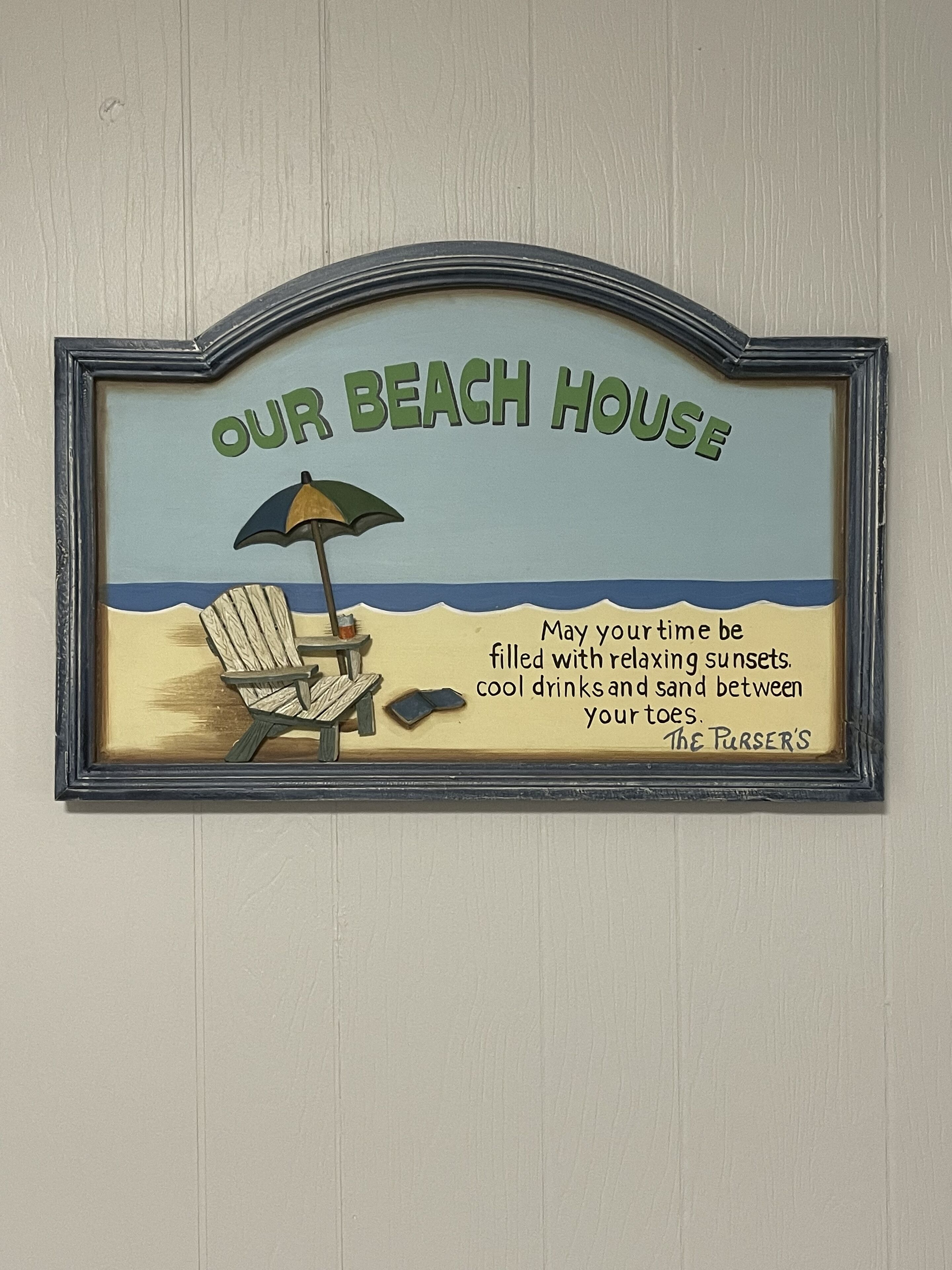 A framed sign with the text "OUR BEACH HOUSE" and a beach scene illustration.