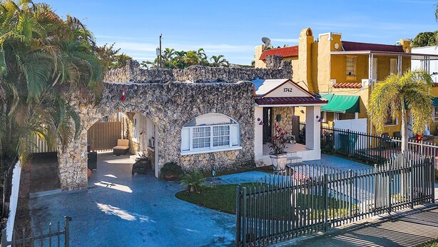 A courtyard with a stone archway, a building with a red roof, and a fenced area. - Little Havana Studio for 4 • Free Parking (Miami)