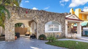 A stone archway leading to a building with a window and a door, a paved driveway, and a small garden area. - Little Havana Studio for 4 • Free Parking (Miami)