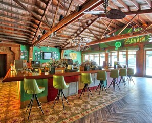 Un bar avec un plafond en bois, des chaises vertes et un sol à motifs.