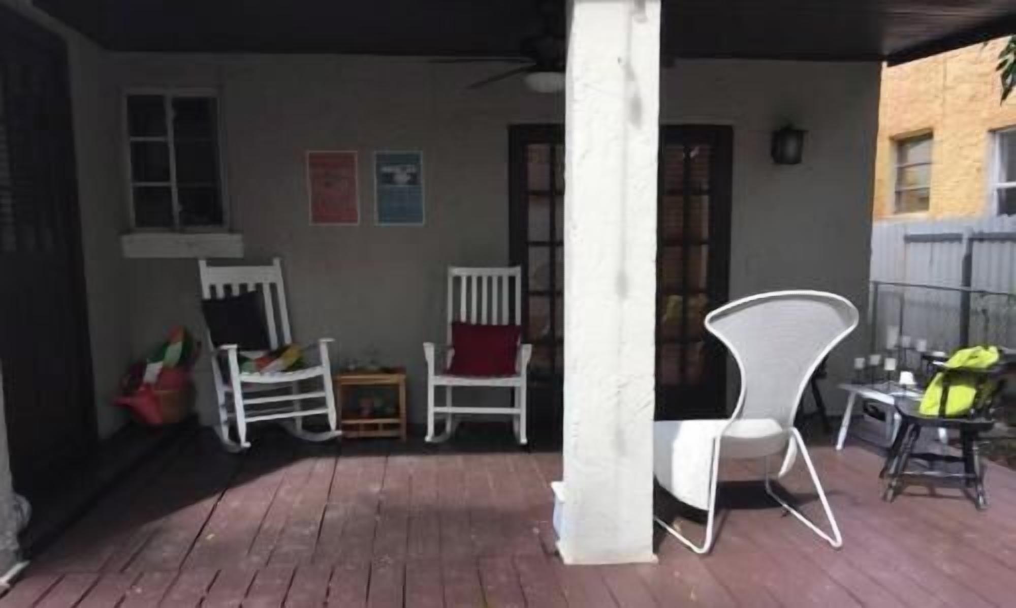 A covered patio area with white chairs, a small table, and a red cushion.