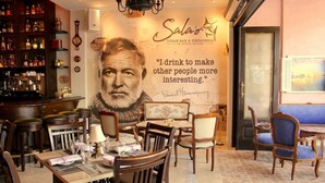 En restaurantindretning med et stort muralmaleri, træmøbler og en bar med flasker.