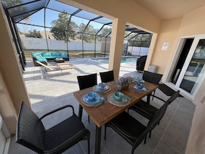 A covered patio with a wooden table set for dining, surrounded by wicker chairs. - 🌴Little Paradise 🌴w/heated pool in PALM COAST Florida (Palm Coast)
