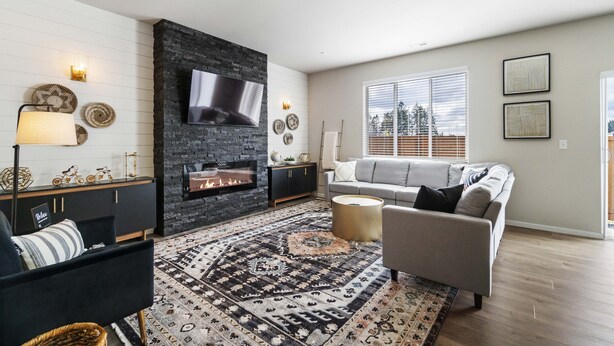 Un salon moderne avec une cheminée, un canapé gris, un tapis à motifs et un téléviseur à écran plat fixé au mur.