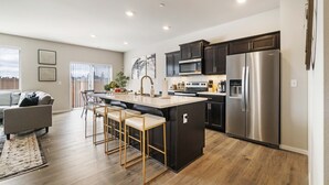 Une cuisine moderne dotée d’un îlot central, de meubles de couleur sombre, d’appareils électroménagers en acier inoxydable et d’un coin repas avec des tabourets de bar.