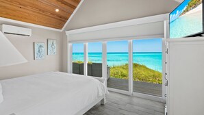 A bedroom with a large bed, a TV, and a view of the ocean. - Shades of Blue a luxury home on private beachfront sleeps 20ppl, chef, boat tour (Forbes Hill)