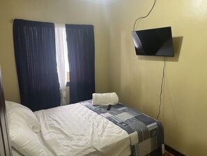 A hotel room with a single bed, a flat-screen TV mounted on the wall, and a window with curtains. - Luxurious Central Apt / 5 min from the Airport (Alajuela)