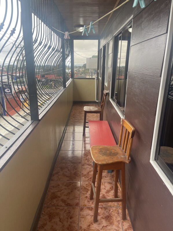 A balcony with two wooden chairs and a red bench, a metal railing, and a view of the cityscape. - Luxurious Central Apt / 5 min from the Airport (Alajuela)