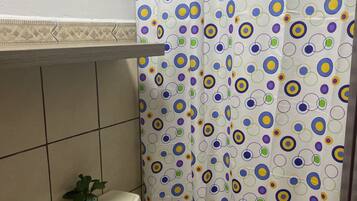 A bathroom with a toilet, a shower curtain with a colorful circular pattern, a small potted plant, and a wall-mounted light fixture.