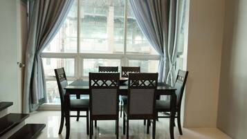 A dining area with a table and chairs, large windows with curtains, and a view of buildings outside.