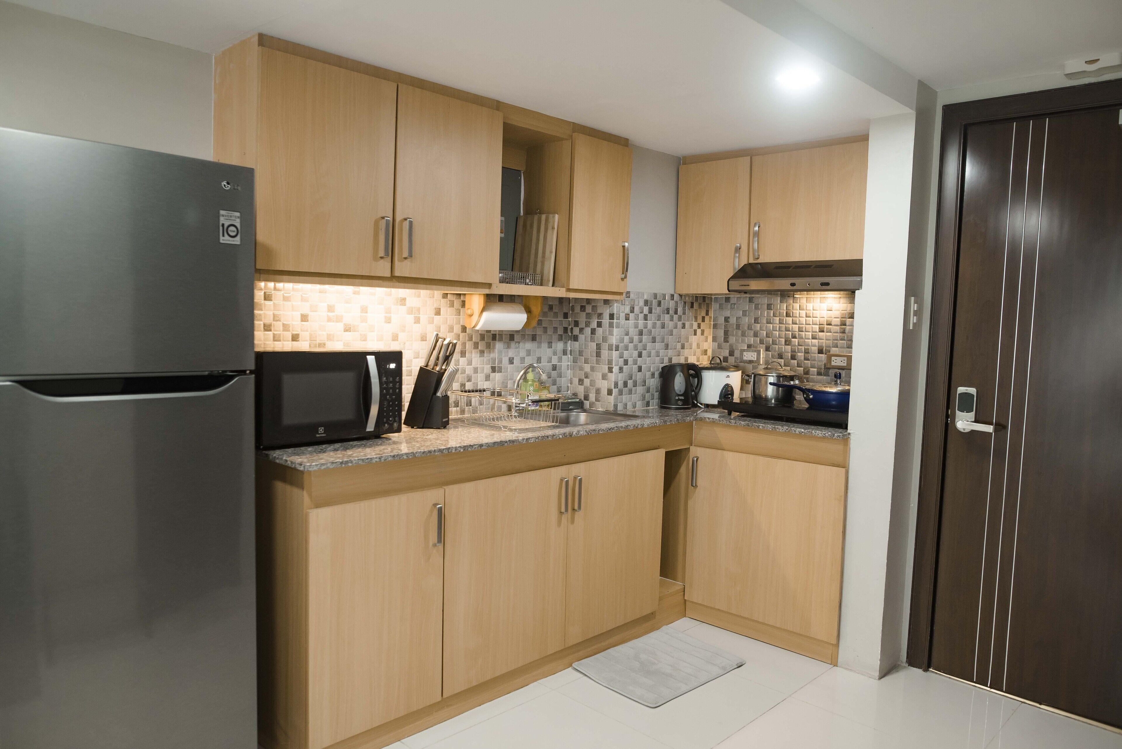 A modern kitchen with wooden cabinets, a stainless steel refrigerator, a microwave, and a sink.