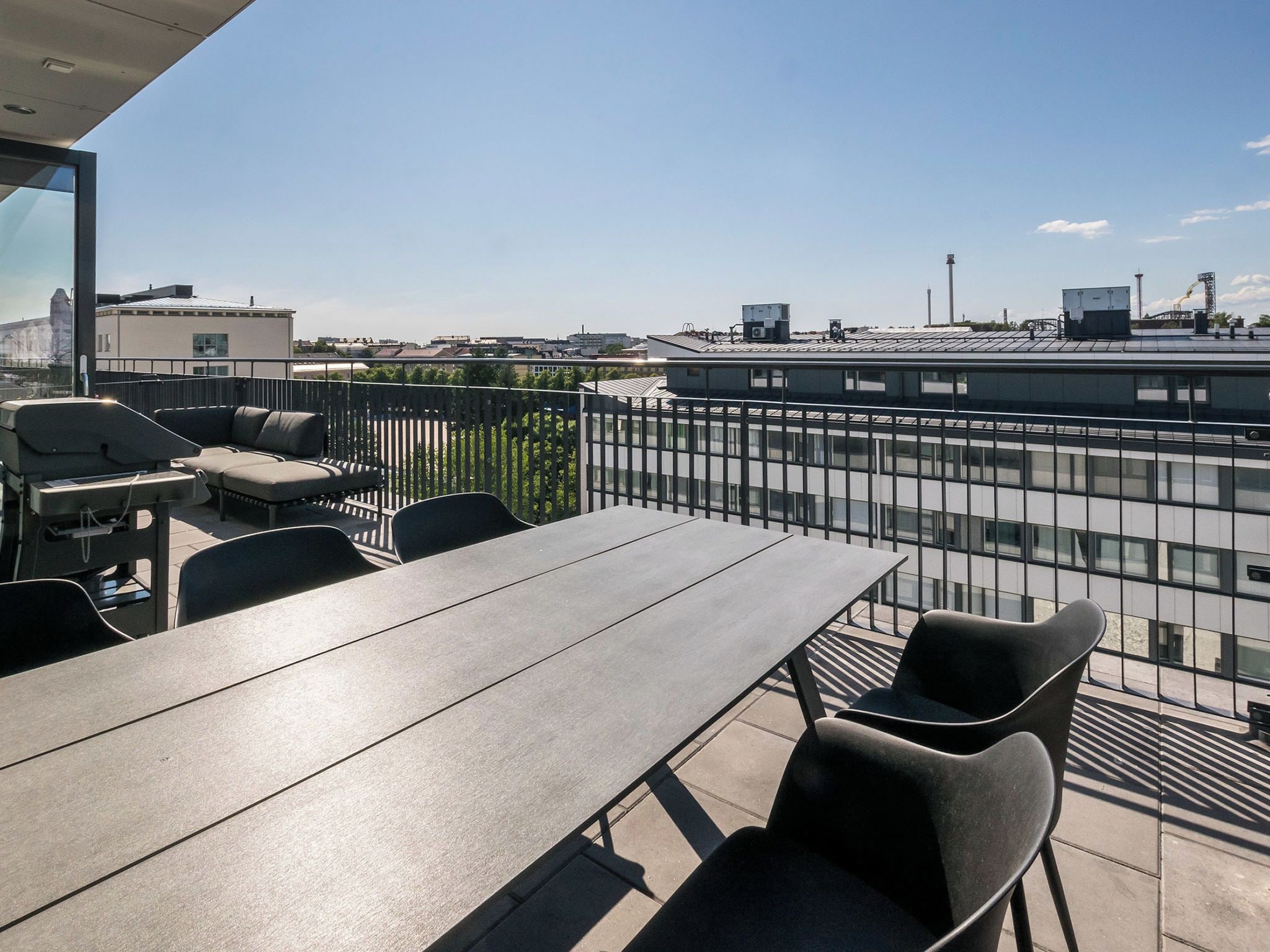 An outdoor terrace with a table and chairs, a view of the cityscape, and a metal fence.