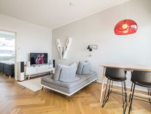 A modern living room with a grey sofa, a wooden dining table with two chairs, a television, and a red pendant light. - Helsinki rooftop by Interhome (Helsinki)
