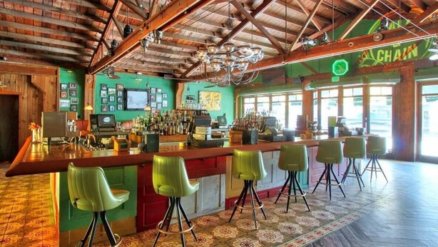 Een bar met een houten plafond, groene stoelen en een patroon vloer.