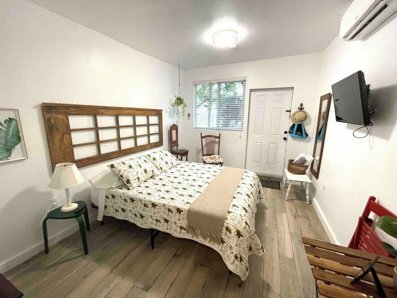 Un dormitorio con cama, mesita de noche, sillón, televisor y ventana.