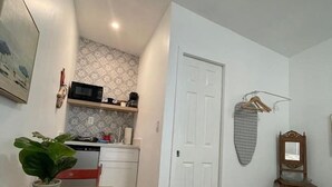Een compacte kamer met kitchenette, een eethoek met tafel en stoelen, een bed en een klein houten bijzettafeltje.