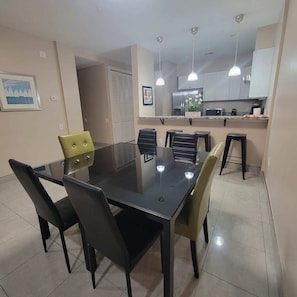 A modern kitchen with a central island, overhead pendant lighting, and a dining area with a glass table and chairs. - Jellyfish 2 BR Oceanfront Condo with Pool (Myrtle Beach)
