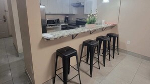 A modern kitchen with white cabinets, a granite countertop, and a central island with bar stools. - Jellyfish 2 BR Oceanfront Condo with Pool (Myrtle Beach)