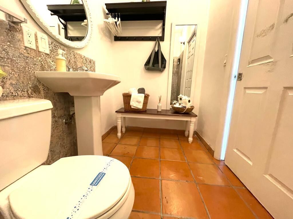 A bathroom with a toilet, sink, and a bench with toiletries.