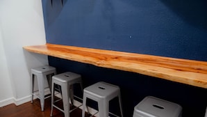 Un'area bar con uno scaffale in legno, tre sgabelli grigi e una parete blu scuro.