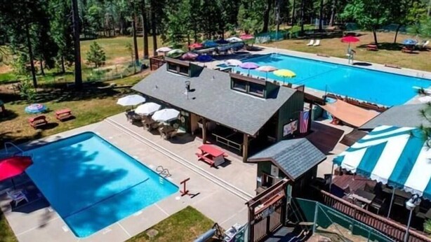 A large outdoor swimming pool with a separate section for children, surrounded by lounge chairs and umbrellas. - Family Retreat! Hot Tub, King Beds & EV Charger (Arnold)