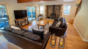 A spacious living room with a stone fireplace, leather sofas, a television, and a wooden coffee table. - Family Retreat! Hot Tub, King Beds & EV Charger (Arnold)