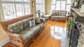 A cozy living room with wicker sofas, a fireplace, and large windows.