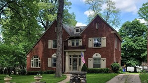 A two-story brick house with a stone entrance, a front porch, and a flag.