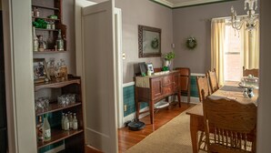 A dining area with a wooden table and chairs, a chandelier, and a bookshelf with various items.