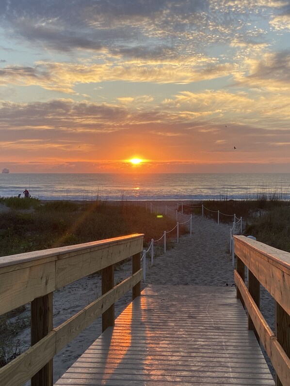 A wooden boardwalk leading to a beach with a sunset in the background.