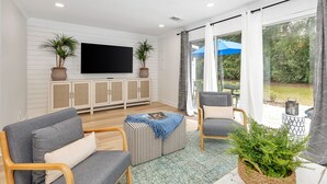 Ein modernes Wohnzimmer mit Fernseher, zwei Sofas, einem Couchtisch und einem großen Fenster mit Vorhängen.