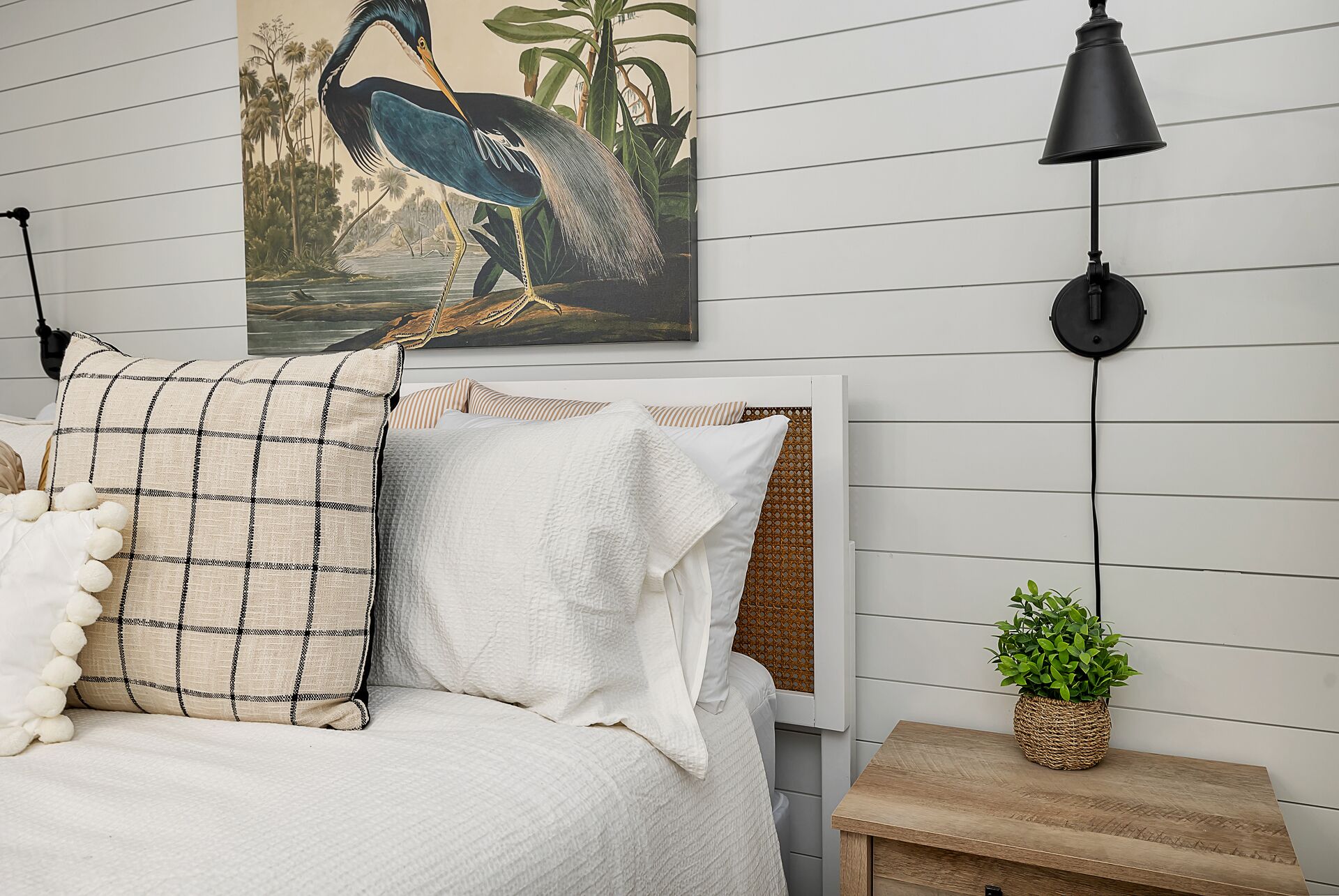 Une chambre à coucher avec un lit, un tableau représentant un oiseau, une lampe et une petite plante.