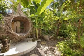 Un jardín con una estructura trenzada, plantas en macetas y senderos de piedra.