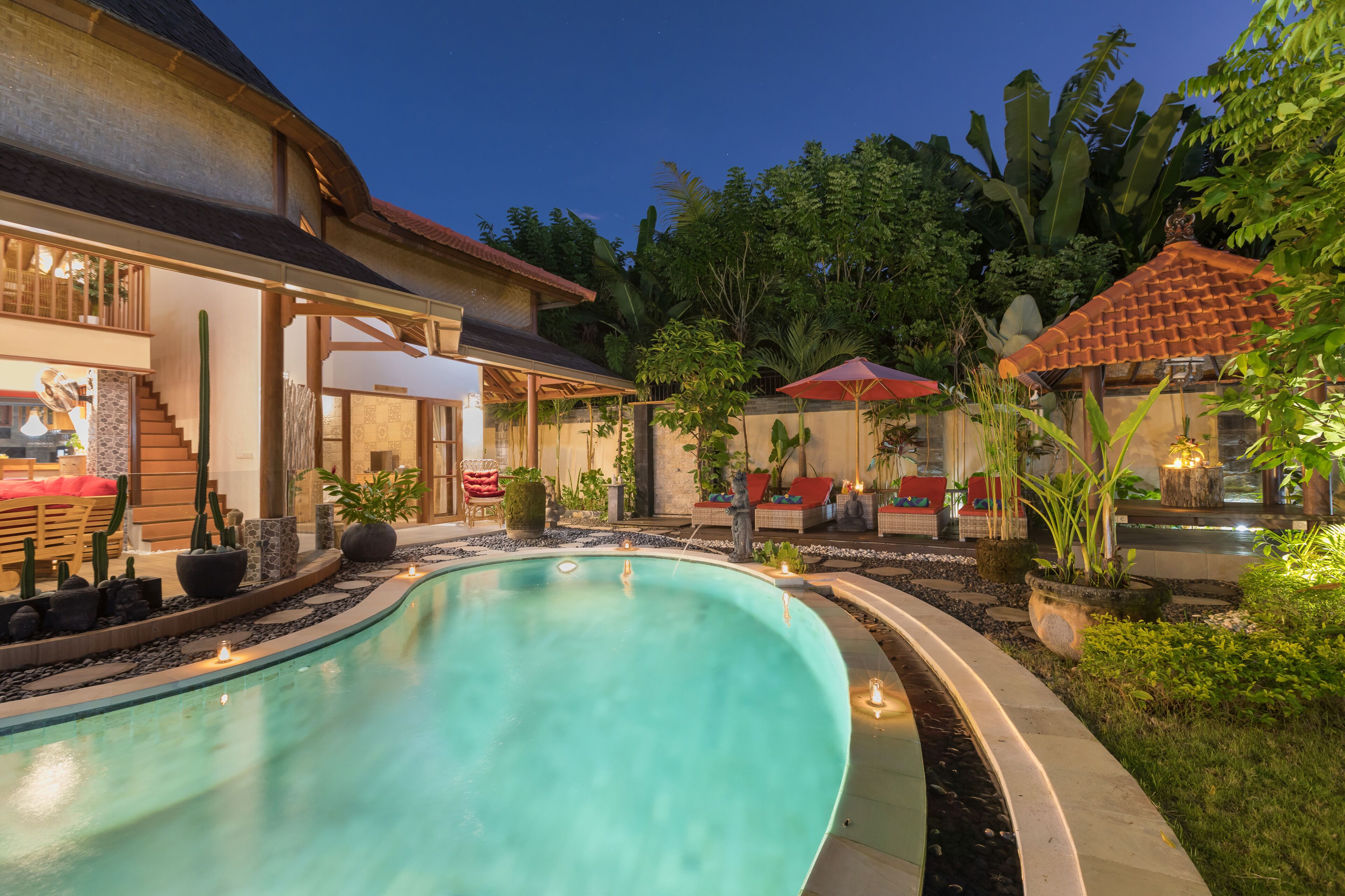 A swimming pool with a curved edge, surrounded by a garden with various plants and a patio area with outdoor seating.