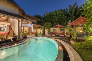 A swimming pool with a curved edge, surrounded by a garden with various plants and a patio area with outdoor seating. -  Villa SoDe Balangan by Nagisa Bali (Jimbaran)