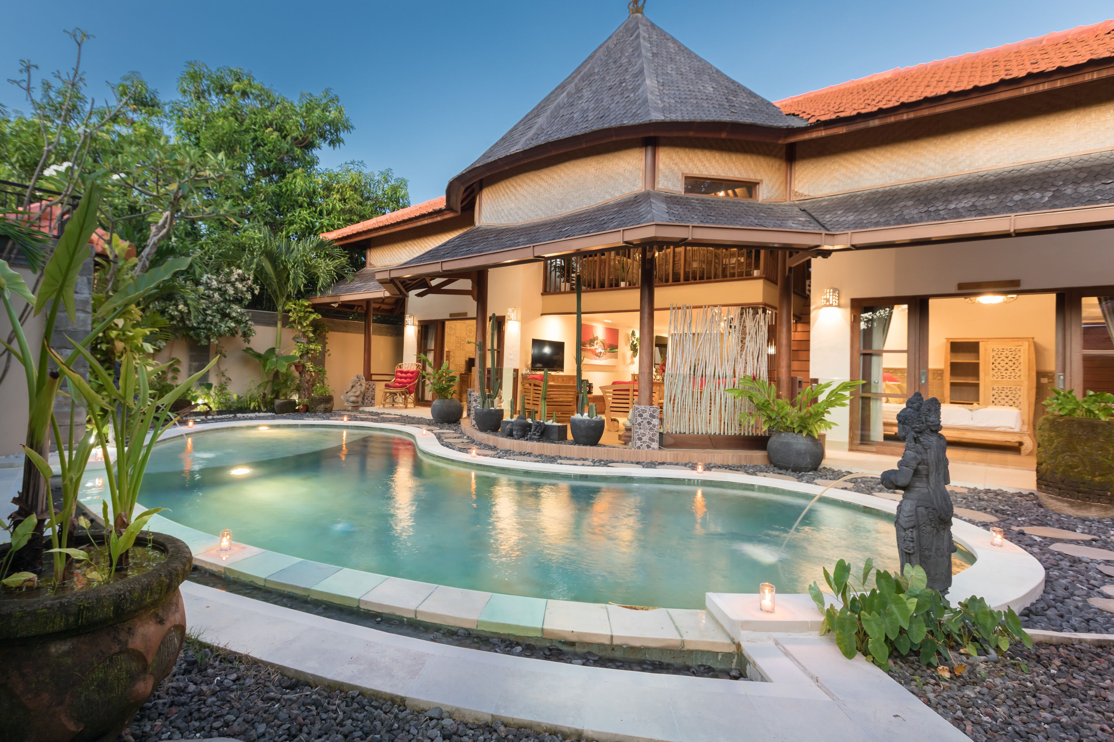 A poolside area with a curved pool, a covered seating area, and a building with a tiled roof.