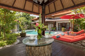A poolside area with a glass table, lounge chairs, and a decorative plant arrangement. -  Villa SoDe Balangan by Nagisa Bali (Jimbaran)