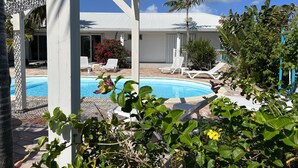 A pool area with lounge chairs, a pergola, and a view of a building with a white roof. - Charming OCEANE studio T1 in guest house with sea view (Collectivity of Saint Martin)