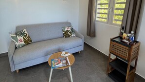 A living room with a grey sofa, a small wooden side table, and a round coffee table. - Charming OCEANE studio T1 in guest house with sea view (Collectivity of Saint Martin)