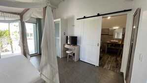A bedroom with a bed, a desk, a TV, and a sliding door leading to a bathroom. - Charming OCEANE studio T1 in guest house with sea view (Collectivity of Saint Martin)
