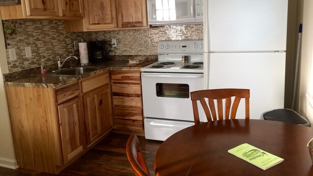 Una cocina con armarios de madera, un refrigerador blanco, un microondas y una estufa. Hay una mesa de comedor con sillas y un menú encima.