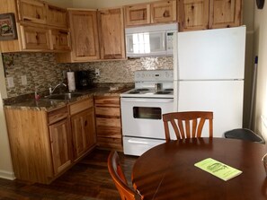 A kitchen with wooden cabinets, a white refrigerator, a microwave, and a stove. There is a dining table with chairs and a menu on it. - Minutes From Shawnee National Forest in Golconda, IL (Golconda)
