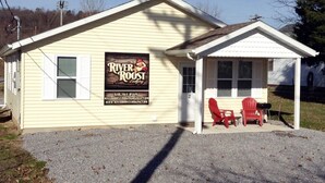 Un pequeño alojamiento con un cartel que dice 'River Roast Lodging'. Cuenta con un porche cubierto y dos sillas Adirondack rojas.