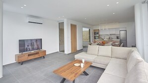 A modern living room with a flat-screen TV, a wooden coffee table, and a beige sofa. - Protaras Vie Bleu Villa VB15 -  a villa that sleeps 7 guests  in 3 bedrooms (Unknown)