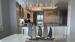 A modern kitchen with white cabinetry, a central island with a sailboat sculpture, and a decorative ceiling with hanging elements.
